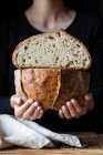Unbekannter zeigt frisches halbiertes Brot mit Samen gegen Holzwand — Stockfoto
