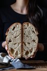 Unrecognizable person showing fresh halved bread with seeds against wooden wall — Stock Photo