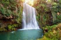 Water falling from rocky cliff at green vibrant forest with moss and grass — Stock Photo