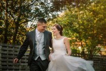 Feliz pareja de recién casados corriendo a lo largo de valla en el jardín - foto de stock
