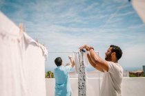 Homens multirraciais pendurando roupas em dia brilhante — Fotografia de Stock