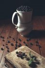 Vintage jag with ripe blackberries on wooden table and leaves on old book — Stock Photo