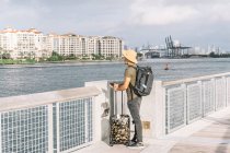 Чоловік з валізою та рюкзаком, який прибуває на берег Маямі, спостерігає за річкою та будівлями в сонячний ранок. — стокове фото