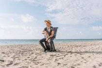 Красивый и подтянутый парень позирует с маленьким чемоданом на пляже в океане — стоковое фото