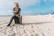 Schöner und fitter Kerl posiert mit kleinem Koffer am Strand — Stockfoto