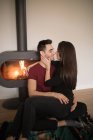 Pleased adult woman in casual clothes looking away and dreaming while sitting on floor and lying on shoulder of boyfriend in love near fireplace on colorful carpet against white wall at home — Stock Photo