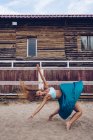 Side view of artistic woman in long wavy skirt dancing and balancing at sandy enclosure by farm barn in daylight — Stock Photo