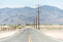 Estrada rural no campo empoeirado com linha de energia e cordilheira remota nos EUA — Fotografia de Stock