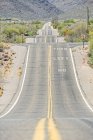 Landstraße auf staubigem Feld mit Hochspannungsleitung und abgelegener Gebirgskette in Tucson, Arizona, USA — Stockfoto