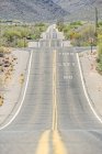 Rural highway at dusty field with power line and remote mountain range in Tucson, Arizona, USA — Stock Photo