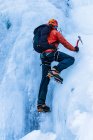 Visão traseira da pessoa em roupas quentes com mochila usando ferramentas para escalar geleira congelada da montanha — Fotografia de Stock