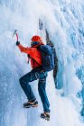 Visão traseira da pessoa em roupas quentes com mochila usando ferramentas para escalar geleira congelada da montanha — Fotografia de Stock