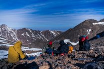 Eine Gruppe von Menschen mit Rucksäcken in warmer Kleidung sitzt an einem sonnigen Tag am felsigen Hang — Stockfoto