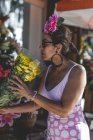 Side view of eccentric curious woman in colorful pink costume picking beautiful bright bouquet at flower shop on sunny day — Stock Photo
