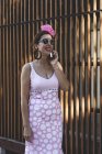 Eccentric woman in colorful pink costume speaking on smartphone while walking along summer street — Stock Photo