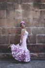 Vue latérale de femme excentrique gaie en costume rose coloré souriant et dansant par mur de briques le jour ensoleillé — Photo de stock