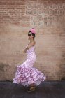 Вид збоку ексцентрична весела жінка в барвистому рожевому костюмі посміхається і танцює на цегляній стіні в сонячний день — стокове фото