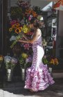 Vista laterale di eccentrica donna curiosa in costume rosa colorato raccogliendo bellissimo bouquet luminoso al negozio di fiori nella giornata di sole — Foto stock