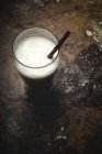 Bicchiere alto di latte bianco con paglia a righe brillanti sul tavolo su sfondo nero — Foto stock