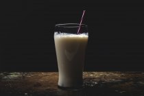 Tall glass of white milk with bright striped straw on table over black background — Stock Photo