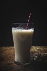 Vidrio de leche blanca con paja brillante en la mesa sobre fondo negro. - foto de stock