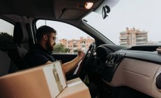 Kurier in Brille bereitet Pakete für den Transport vor, während er tagsüber im Auto sitzt und Kisten markiert — Stockfoto