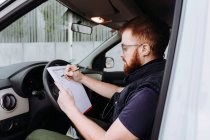 Uomo messa a fuoco e controllo dei documenti mentre seduto dietro il volante in cabina di guida durante il giorno su sfondo sfocato — Foto stock