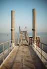 Schmale Seebrücke mit verwitterten Geländern und Fernreisenden in der Nähe ruhigen Meerwassers gegen wolkenlosen Himmel — Stockfoto