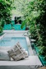 Banco macio com almofadas localizado perto da piscina limpa no jardim verde do hotel em Marraquexe, Marrocos — Fotografia de Stock