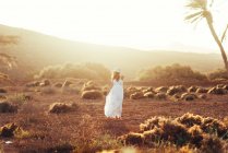 Mujer en vestido blanco en campo seco a la luz del sol - foto de stock