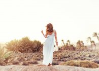 Mulher de vestido branco em campo seco à luz do sol — Fotografia de Stock