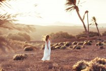 Seitenansicht einer Frau in weißem Kleid, die auf einem Feld mit trockenem Gras in Fuerteventura, Las Palmas, Spanien spaziert — Stockfoto