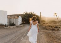 Женщина в белом платье на сельской дороге с сухим полем под солнцем — стоковое фото