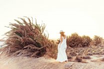 Femme en robe blanche marchant dans un champ sec au soleil en Espagne — Photo de stock