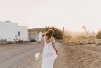 Frau in weißem Kleid auf Landstraße mit trockenem Feld im Sonnenlicht — Stockfoto