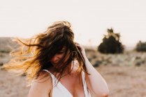 Femme en robe blanche regardant loin avec les cheveux salissants dans le champ sec au soleil — Photo de stock