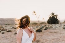 Femme en robe blanche avec des cheveux salissants dans un champ sec au soleil à Fuerteventura, Espagne — Photo de stock