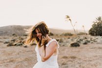 Woman in white dress touching messy hair in dry field in sunlight — Stock Photo