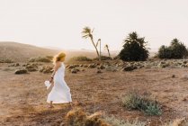 Жінка в білій сукні, що йде в сухому полі на сонячному світлі — стокове фото