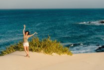 Активная женщина в белых шортах позирует с вытянутыми руками на песчаном пляже — стоковое фото