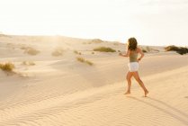 Вид сбоку на спортивную женщину в удобной одежде, бегущую по жаркой сухой пустыне в Фуэртевентуре, Лас-Пальмас, Испания — стоковое фото