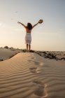 Активная женщина, стоящая со шляпой в вытянутых руках в сухой пустыне — стоковое фото