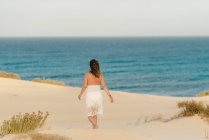 Mujer activa en vestido blanco caminando playa de arena - foto de stock