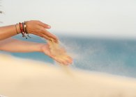 Gelber, sauberer Sand fliegt aus den Händen mit hellen Armbändern von Frauen am Strand von Fuerteventura, Las Palmas, Spanien — Stockfoto