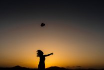 Mulher jogando chapéu na distância para o céu por do sol à noite — Fotografia de Stock