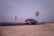 Blaues Auto schnell auf der Straße mit runden Schildern auf hölzernen Säulen entlang des Ozeans in Fuerteventura, Las Palmas, Spanien — Stockfoto