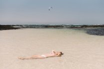 Woman in swimsuit lying in water on seashore — Stock Photo