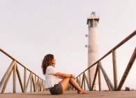Frau sitzt auf Brücke zum Leuchtturm und schaut weg — Stockfoto