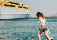 Mulher encaracolada olhando para o navio na água na praia — Fotografia de Stock
