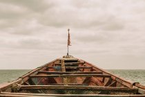 Bateau vieilli avec pavillon flottant sur l'eau de mer ondulante contre ciel nuageux en Gambie — Photo de stock
